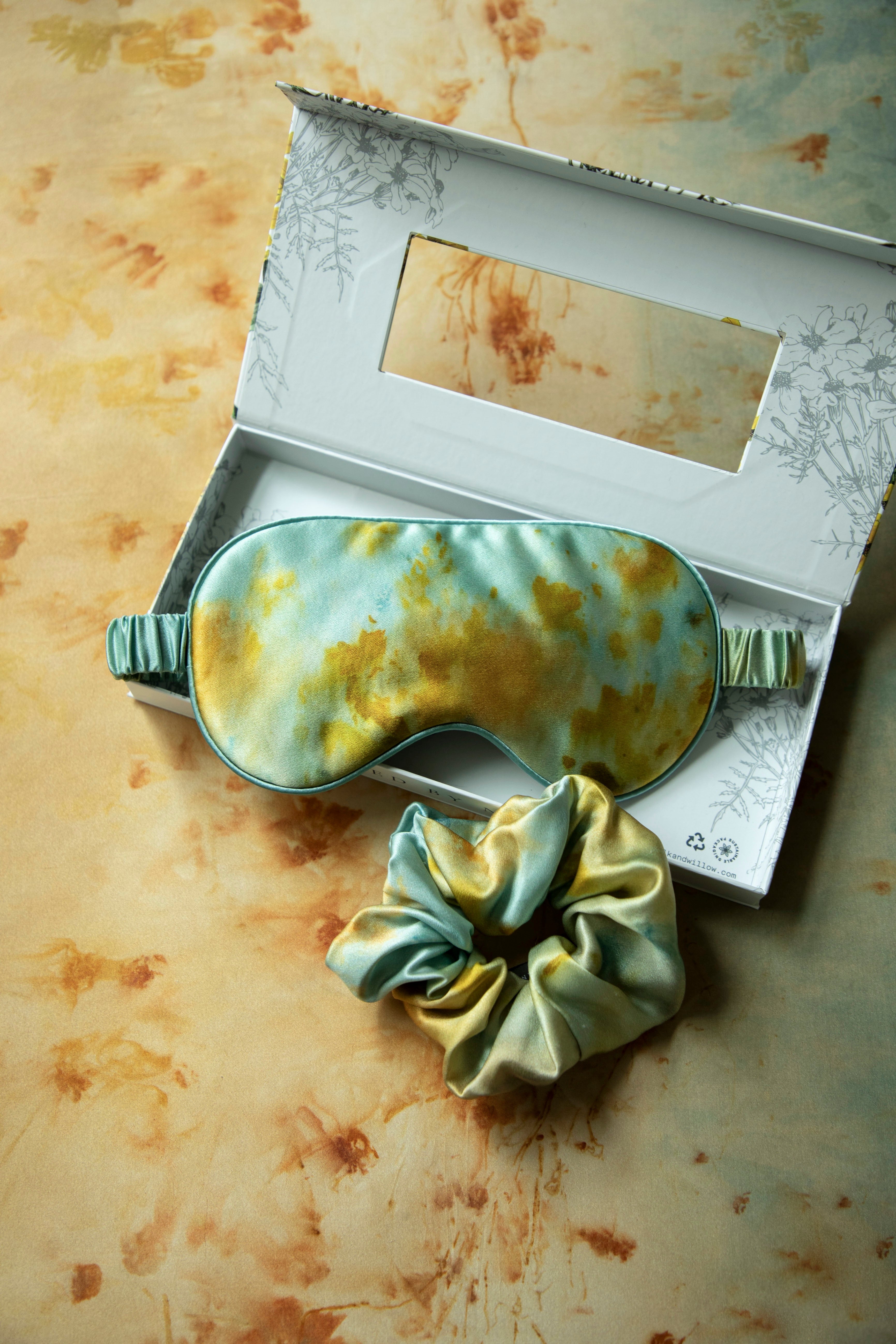 Sleep mask and scrunchie set with vintage-style packaging on a textured surface