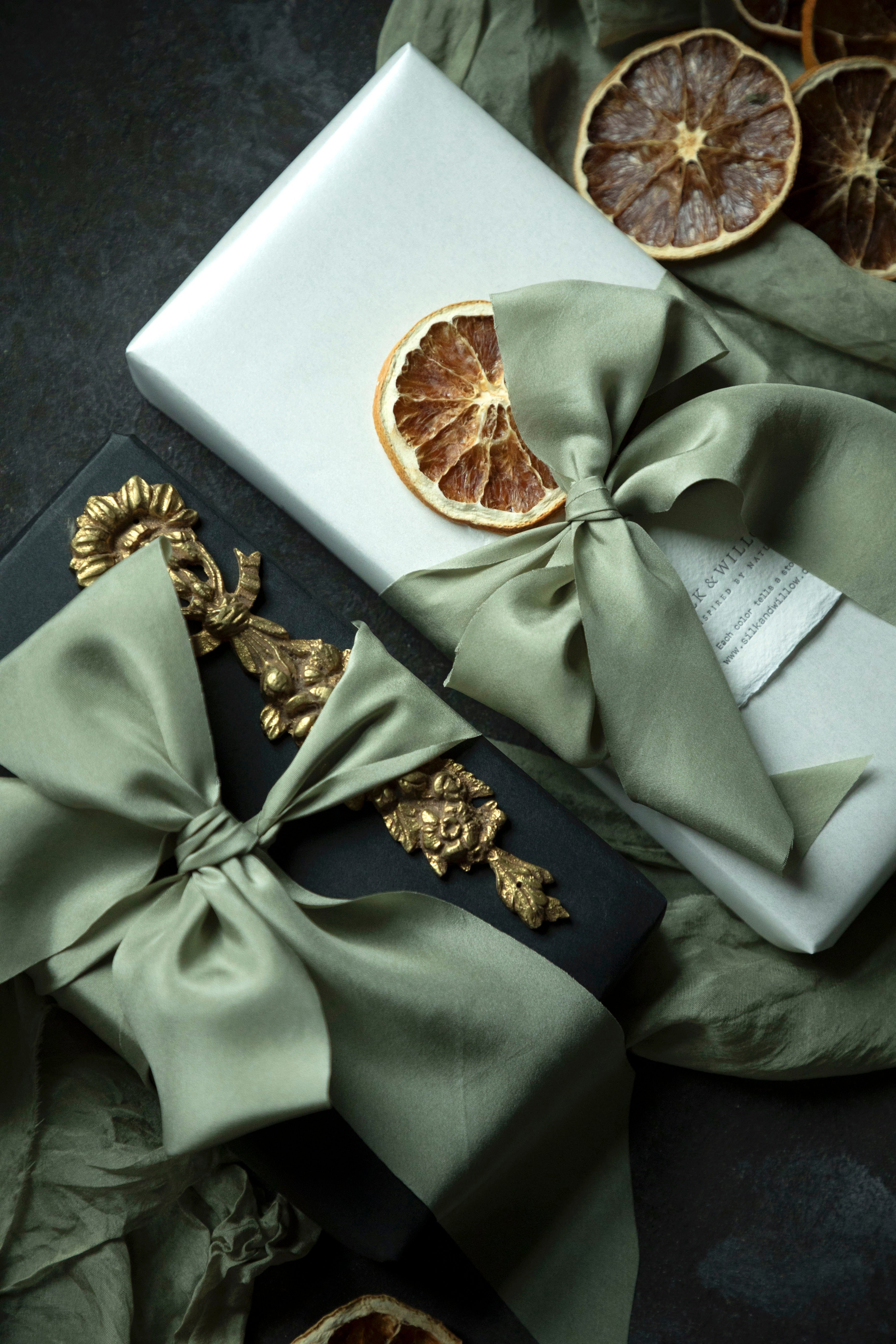 Gifts wrapped in green ribbons with dried oranges on a dark surface