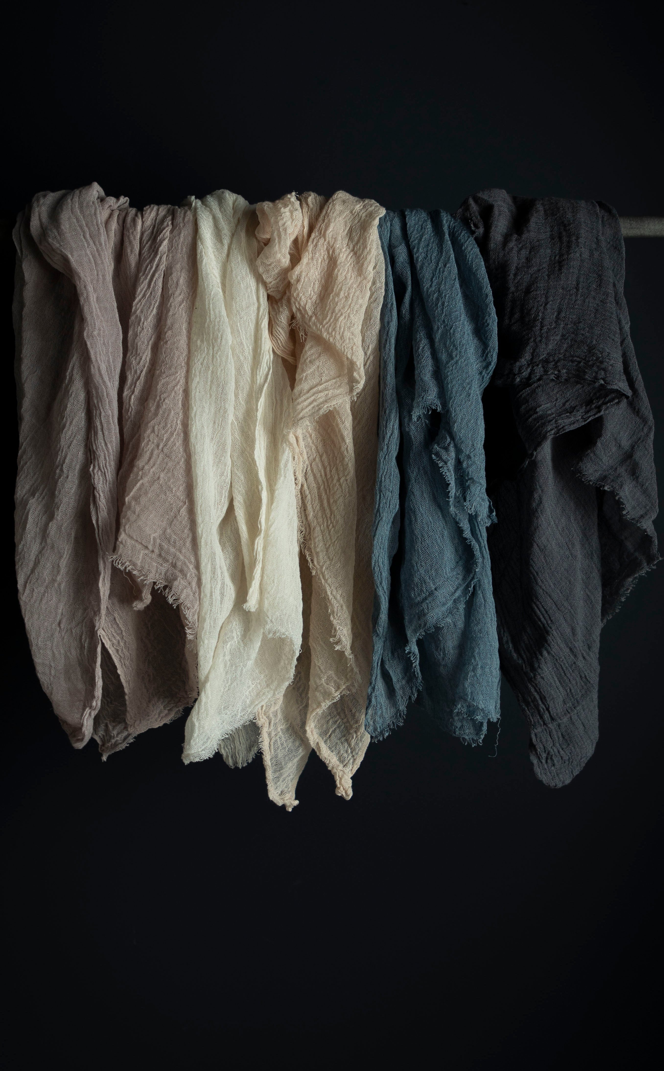 A selection of six handloomed cotton table runners in various colors, hanging against a dark background, showcasing their textures and hues.