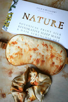 Silk and Willow Nature botanical print silk restorative sleep mask and hair scrunchie set on a textured surface.