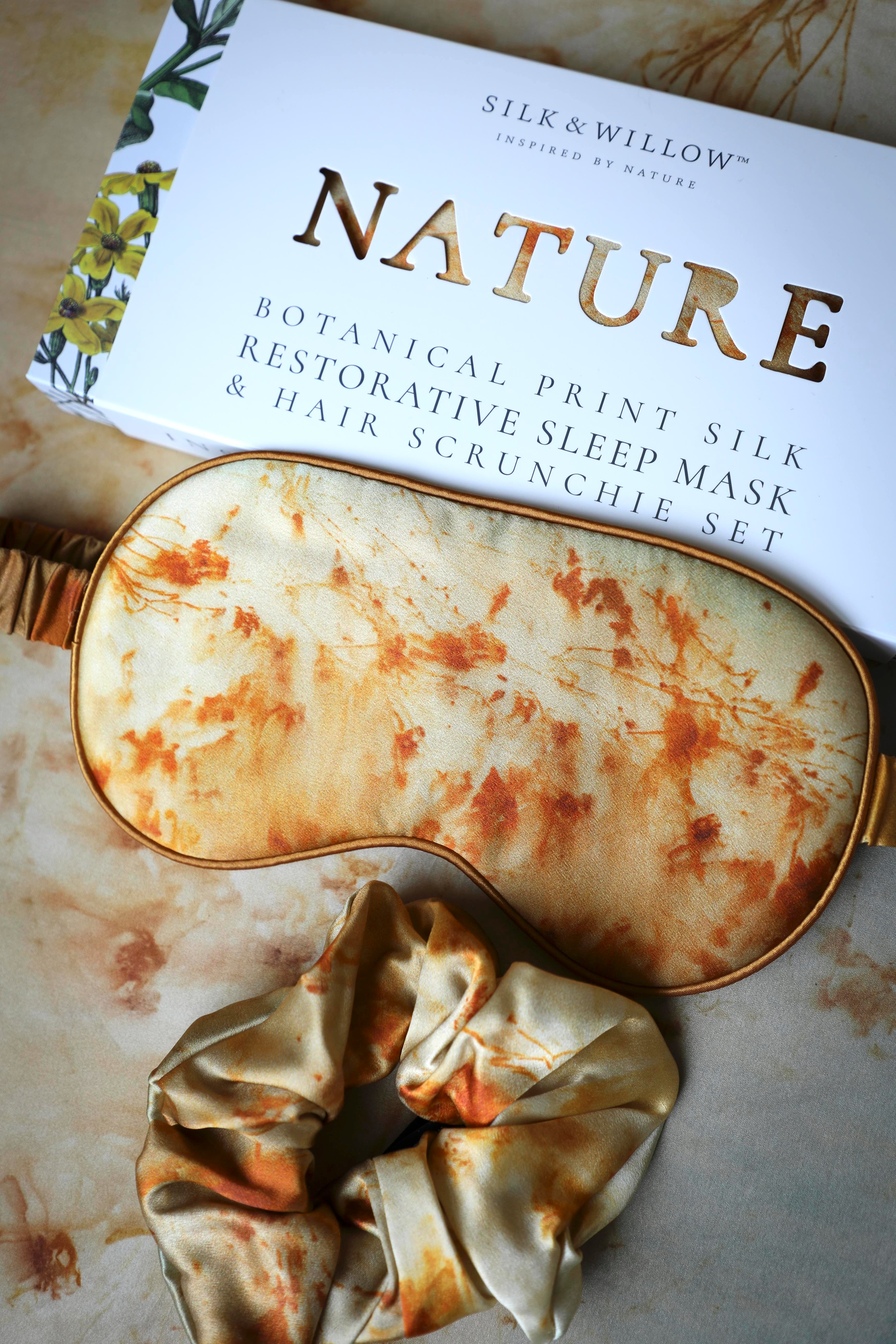 Silk and Willow Nature botanical print silk restorative sleep mask and hair scrunchie set on a textured surface.