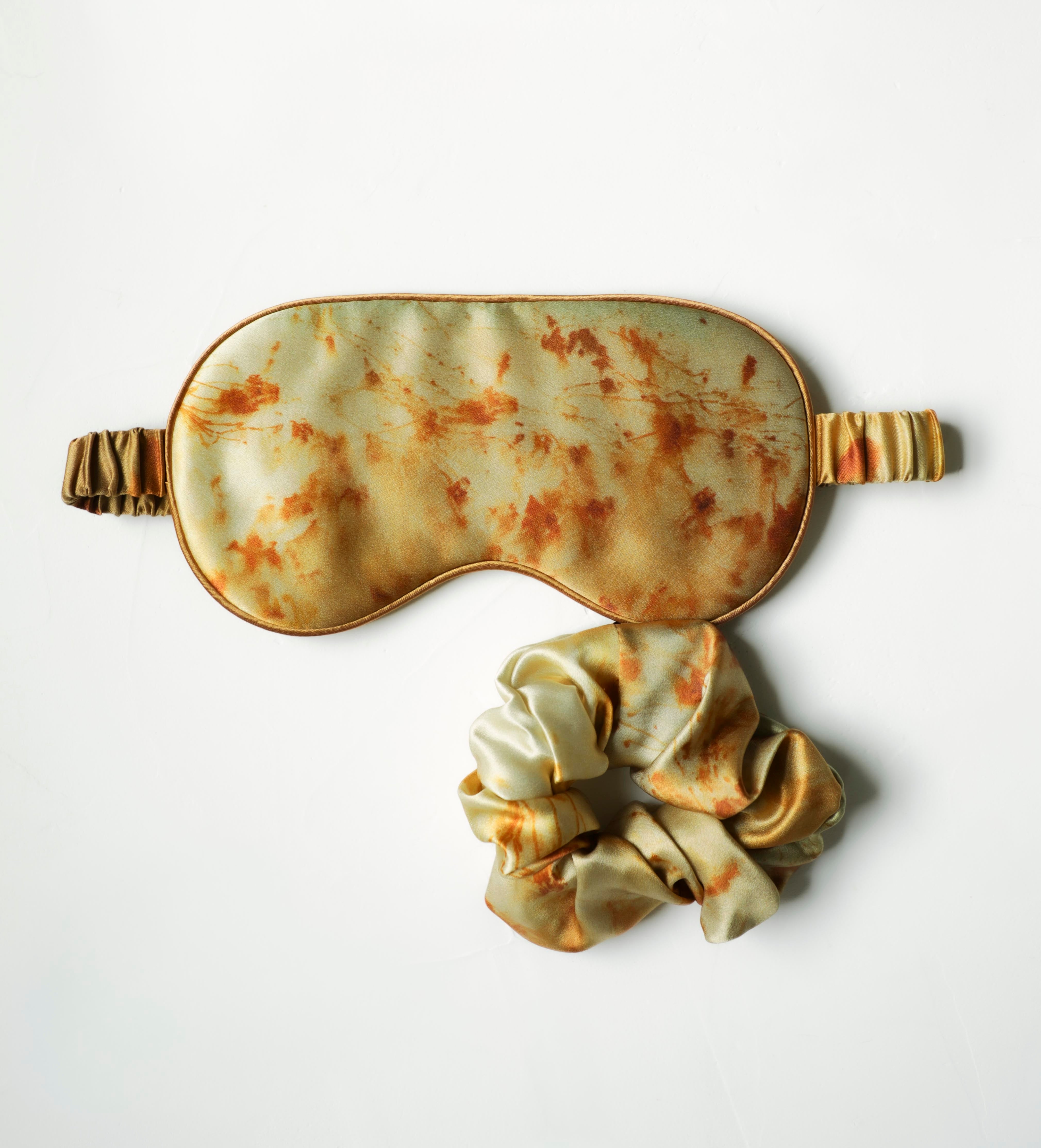 Sleep mask and scrunchie set with a vintage, rust-like pattern on a white background