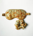 Sleep mask and scrunchie set with a vintage, rust-like pattern on a white background