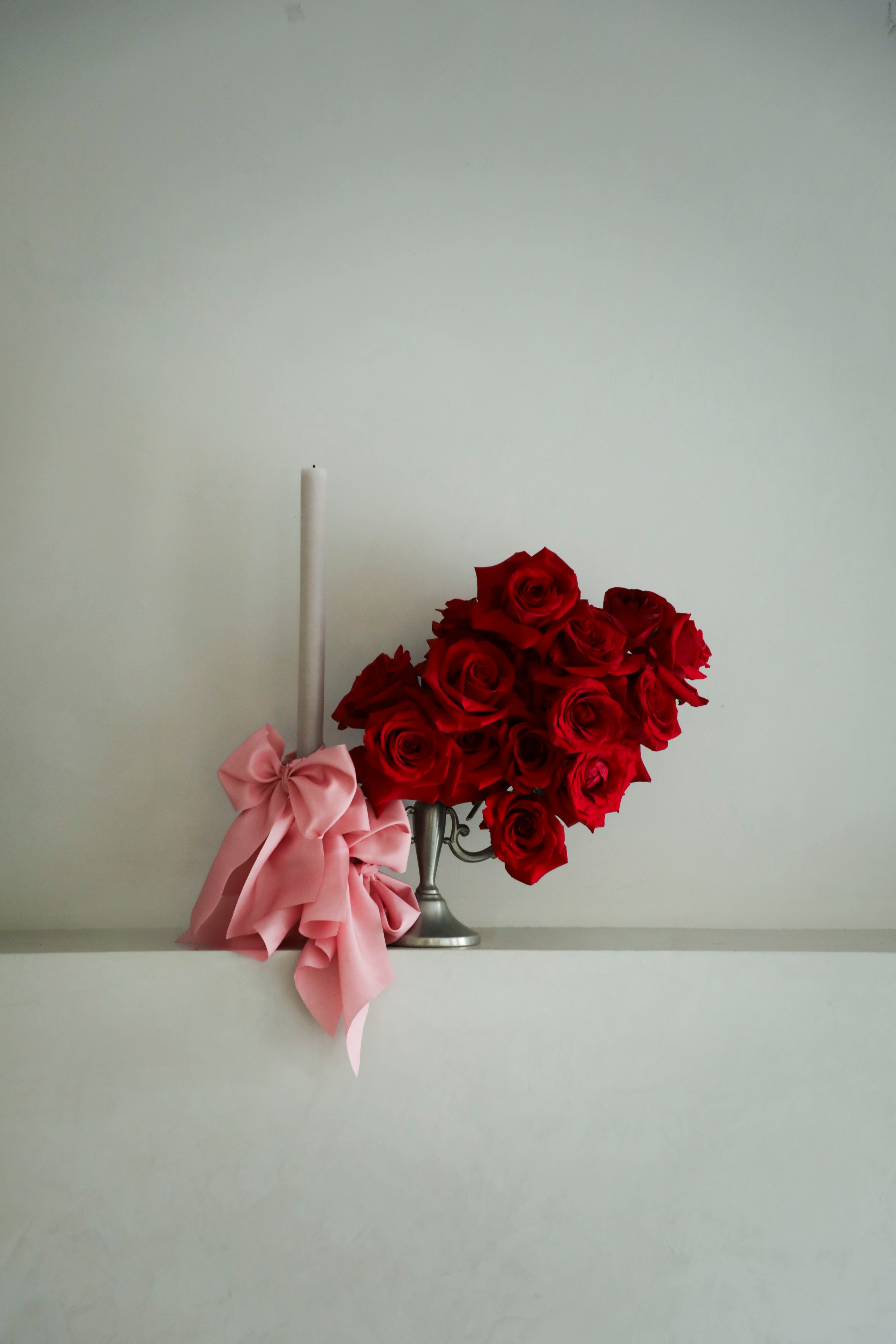 Red roses in a silver vase with a pink bow on a white surface against a light gray background
