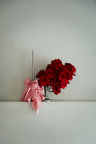 Red roses in a silver vase with a pink bow on a white surface against a light gray background