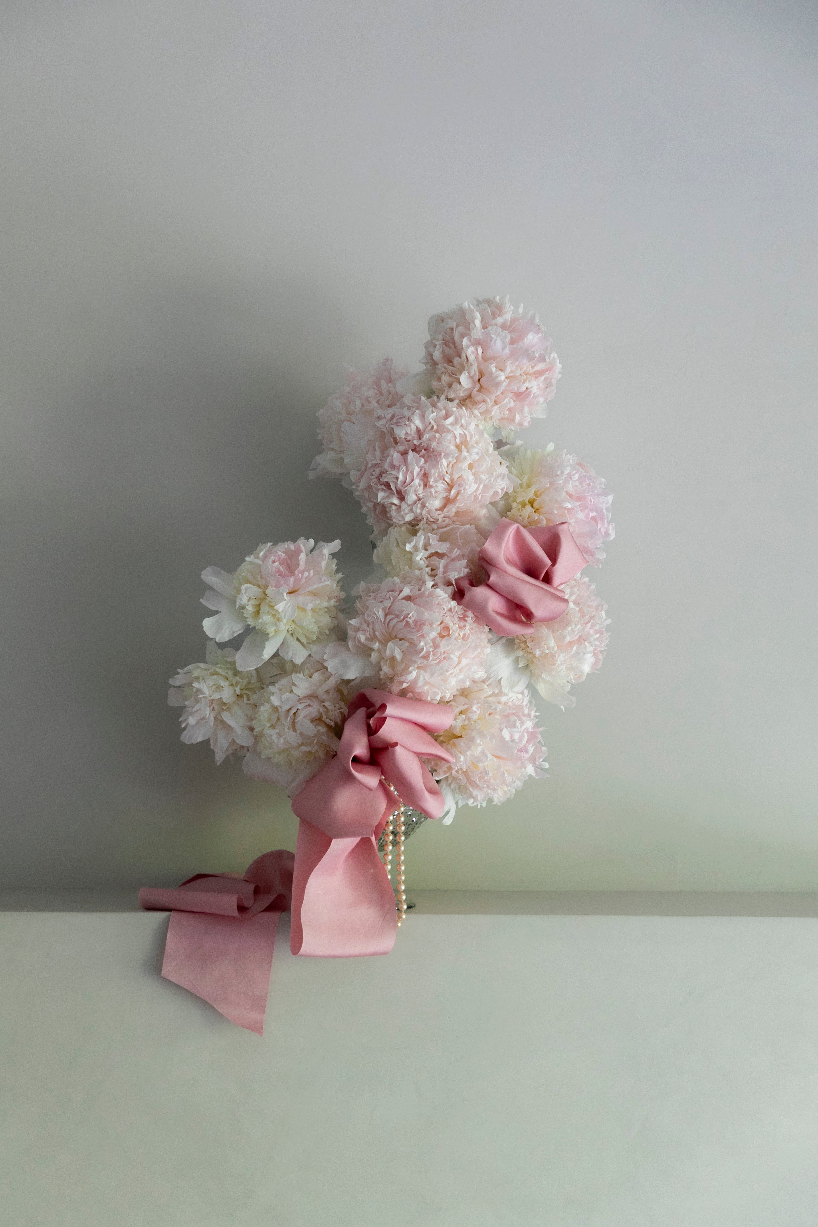 Decorative floral arrangement with peonies and pink ribbons on a plain background