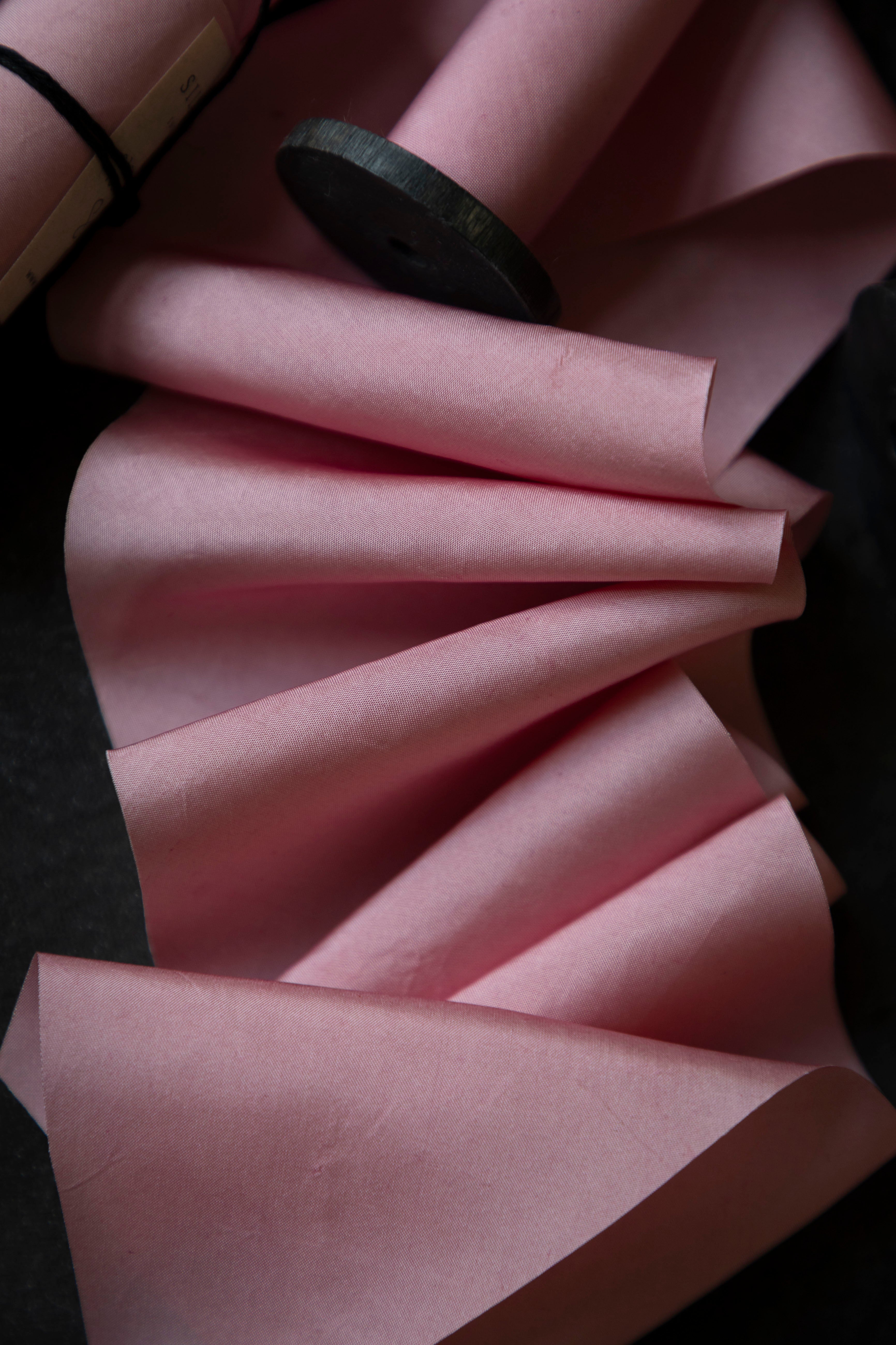 Pink fabric with a wooden spool on a dark background