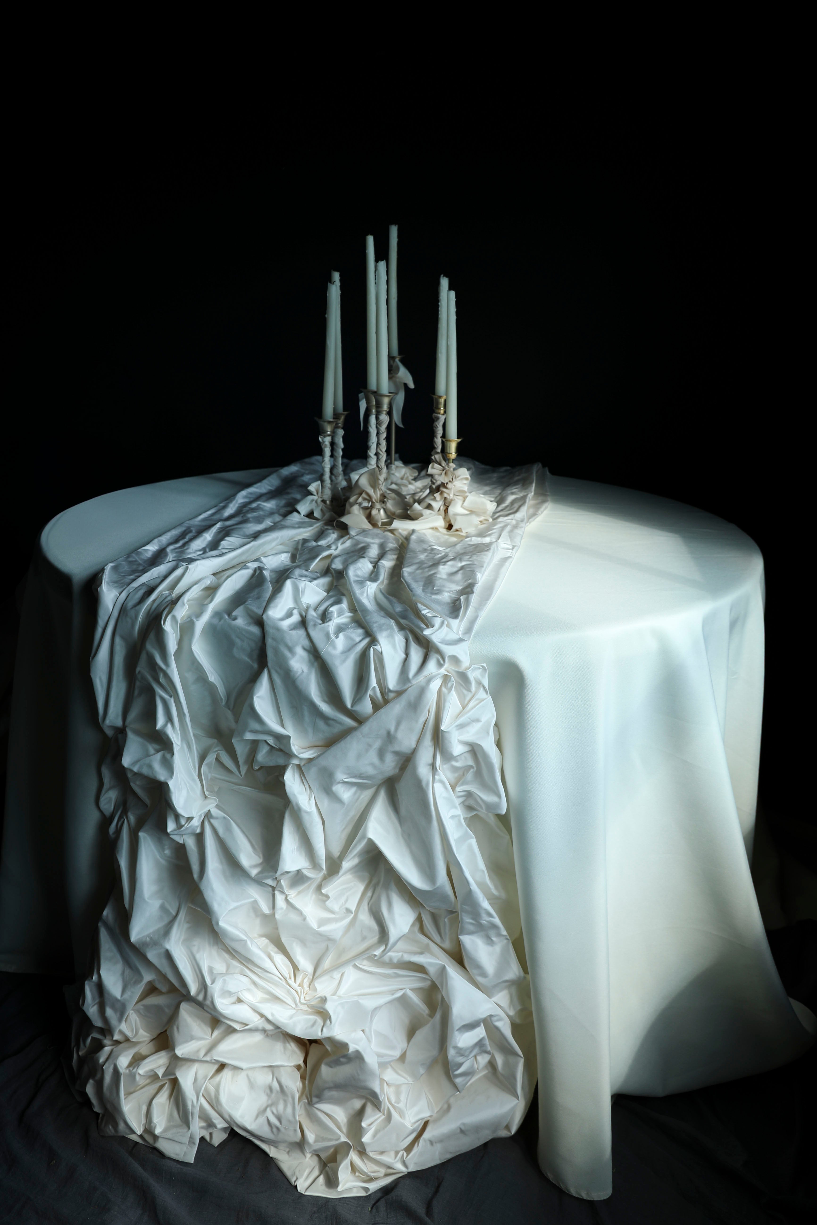 Decorative table with ruffled white tablecloth and candles against a black background