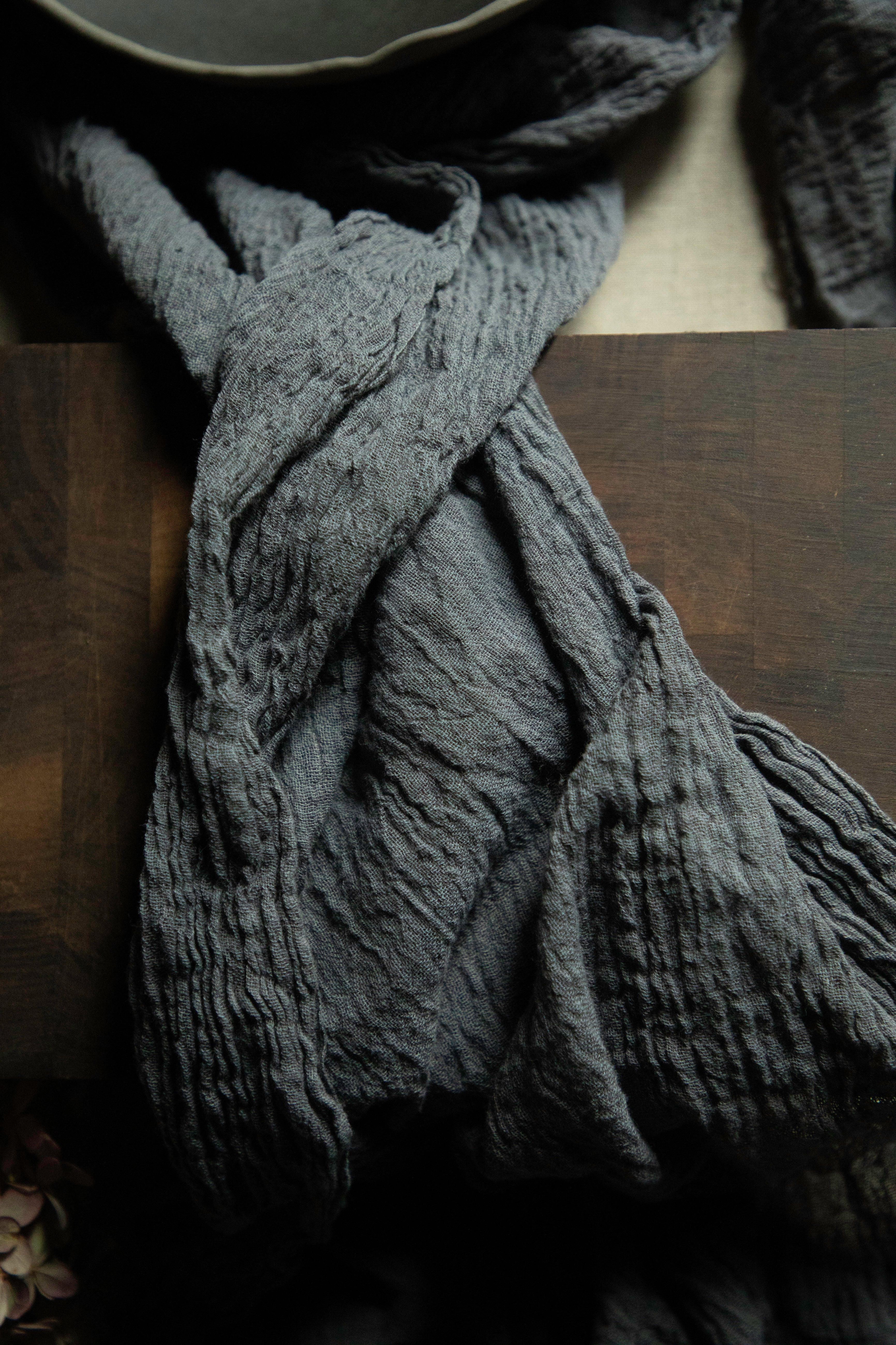 A dark gray crinkled gauze scarf draped over a dark wooden surface.
