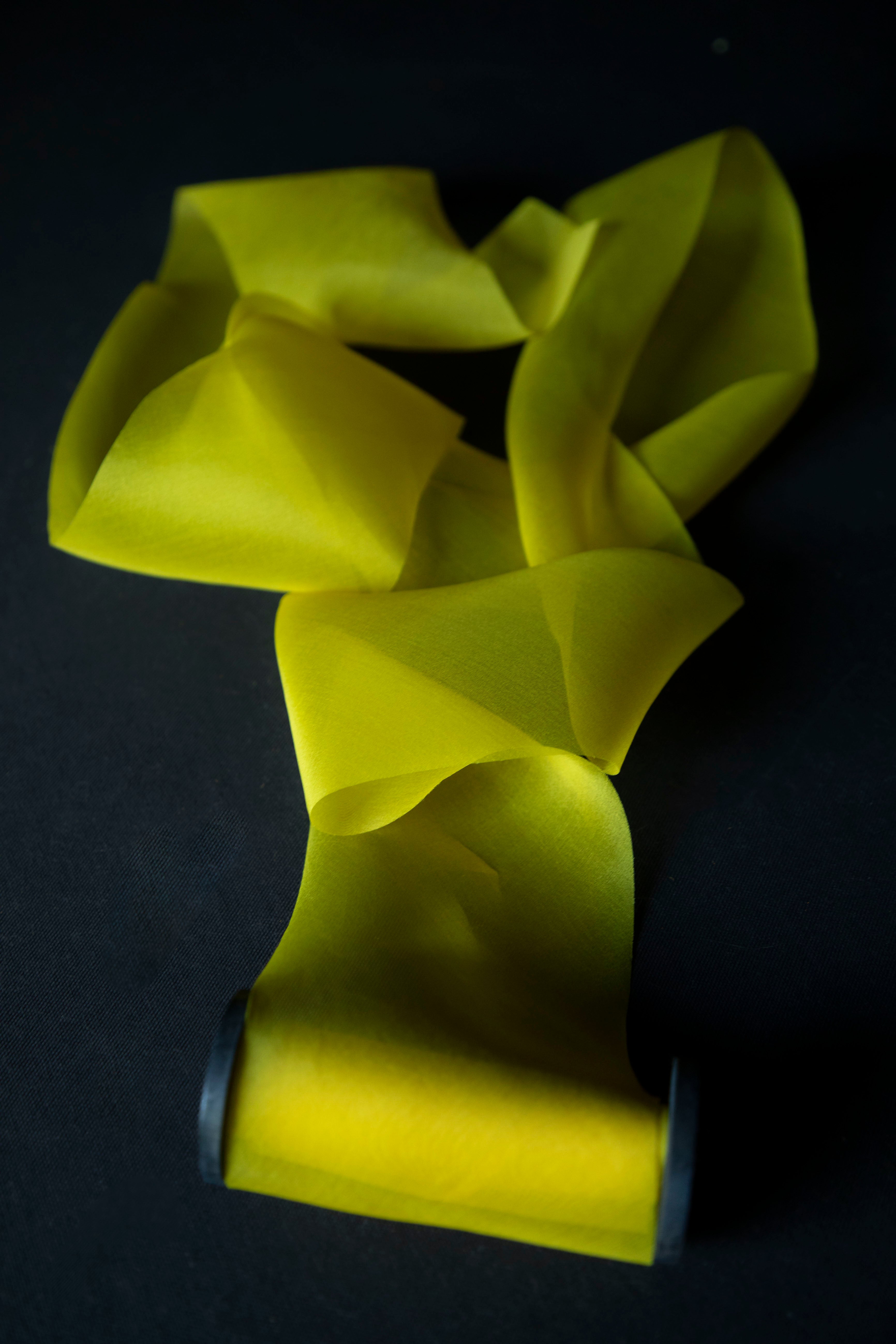 Bright yellow sheer silk ribbon on a dark black background.