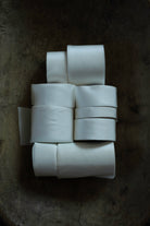 A stack of white fabric ribbon rolls arranged on a dark, textured surface.
