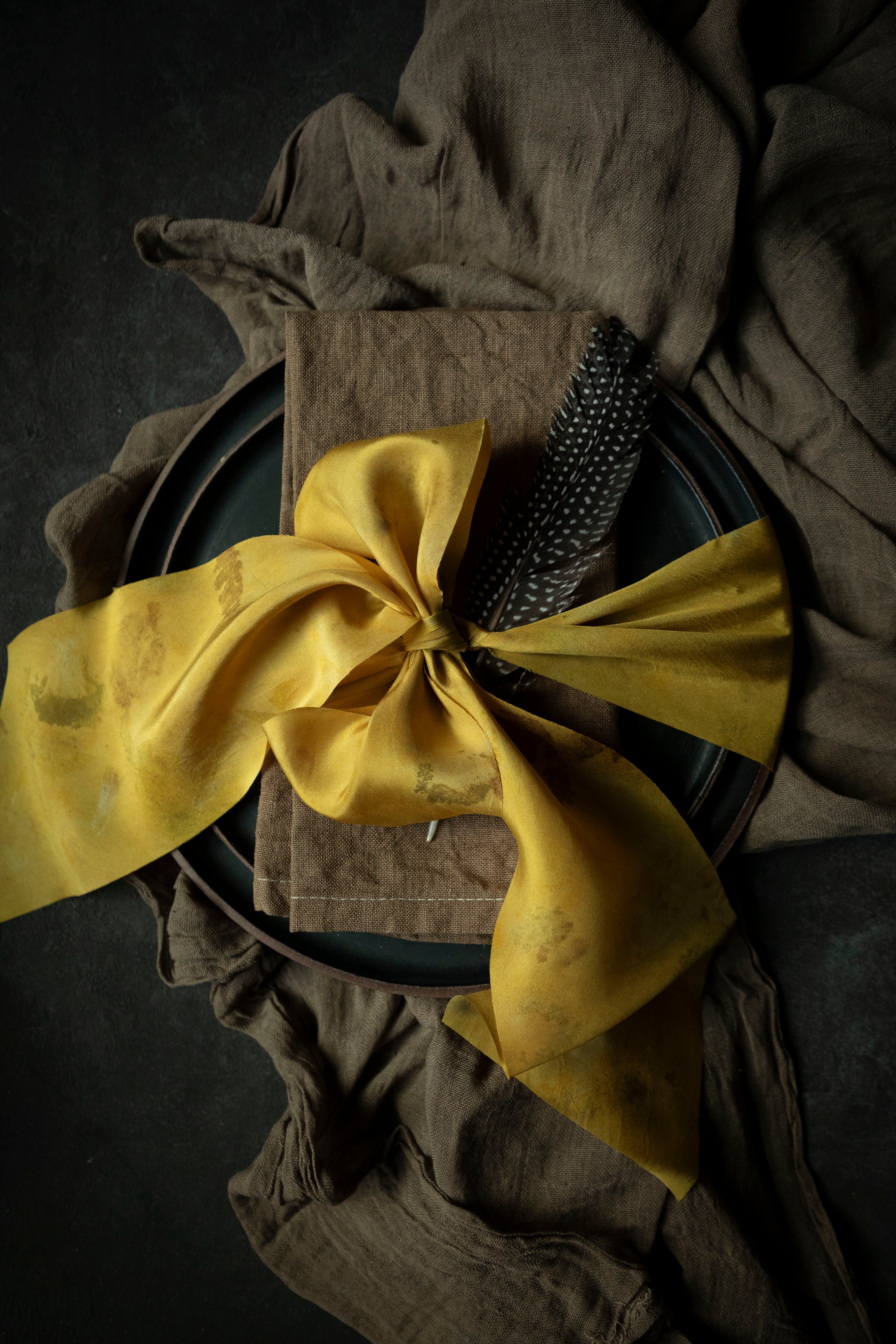 walnut dyed napkin on place setting tied with a yellow ribbon on a black background