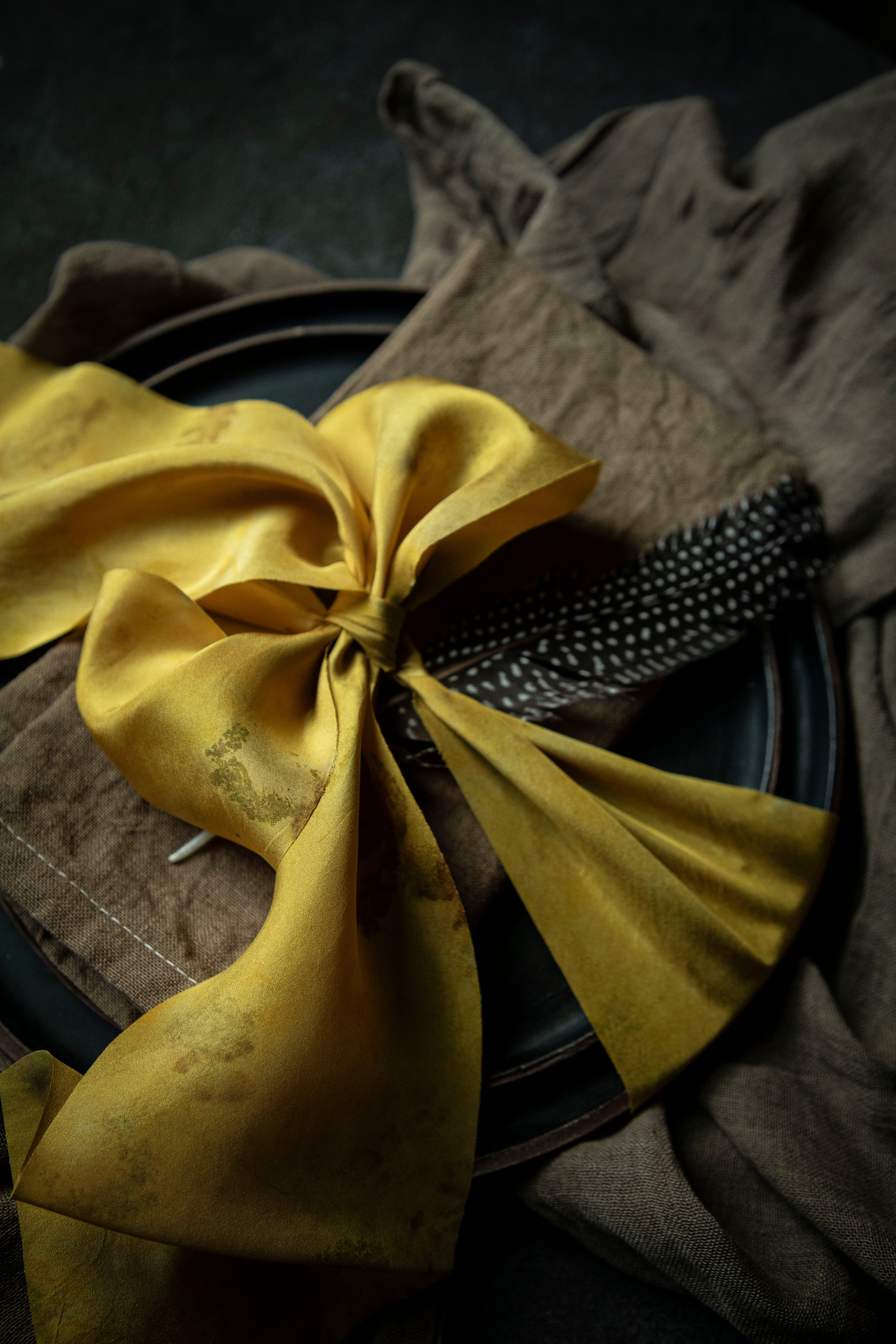 walnut dyed napkin on place setting tied with a yellow ribbon on a black background