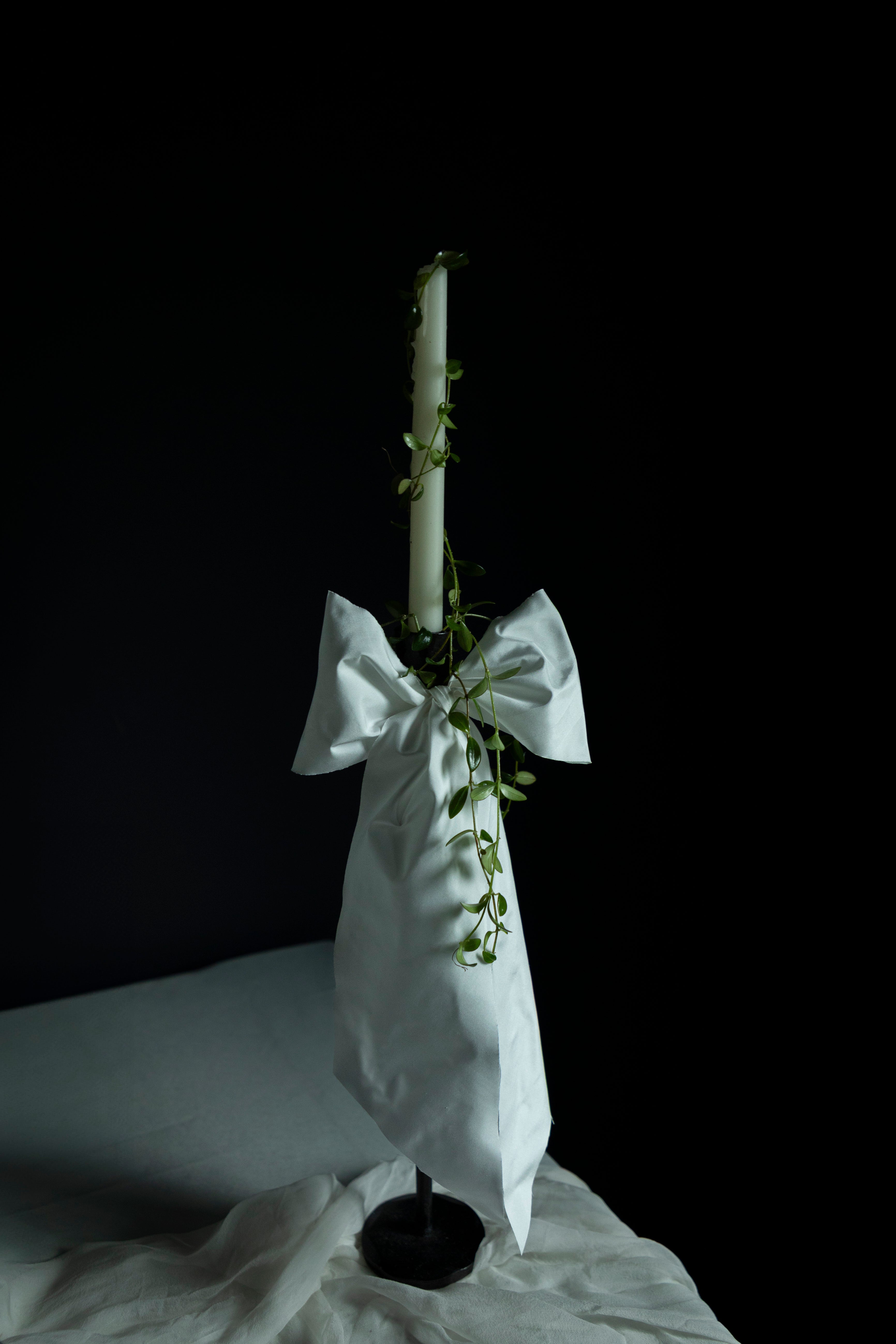 White candle in a holder with a decorative bow on a dark background