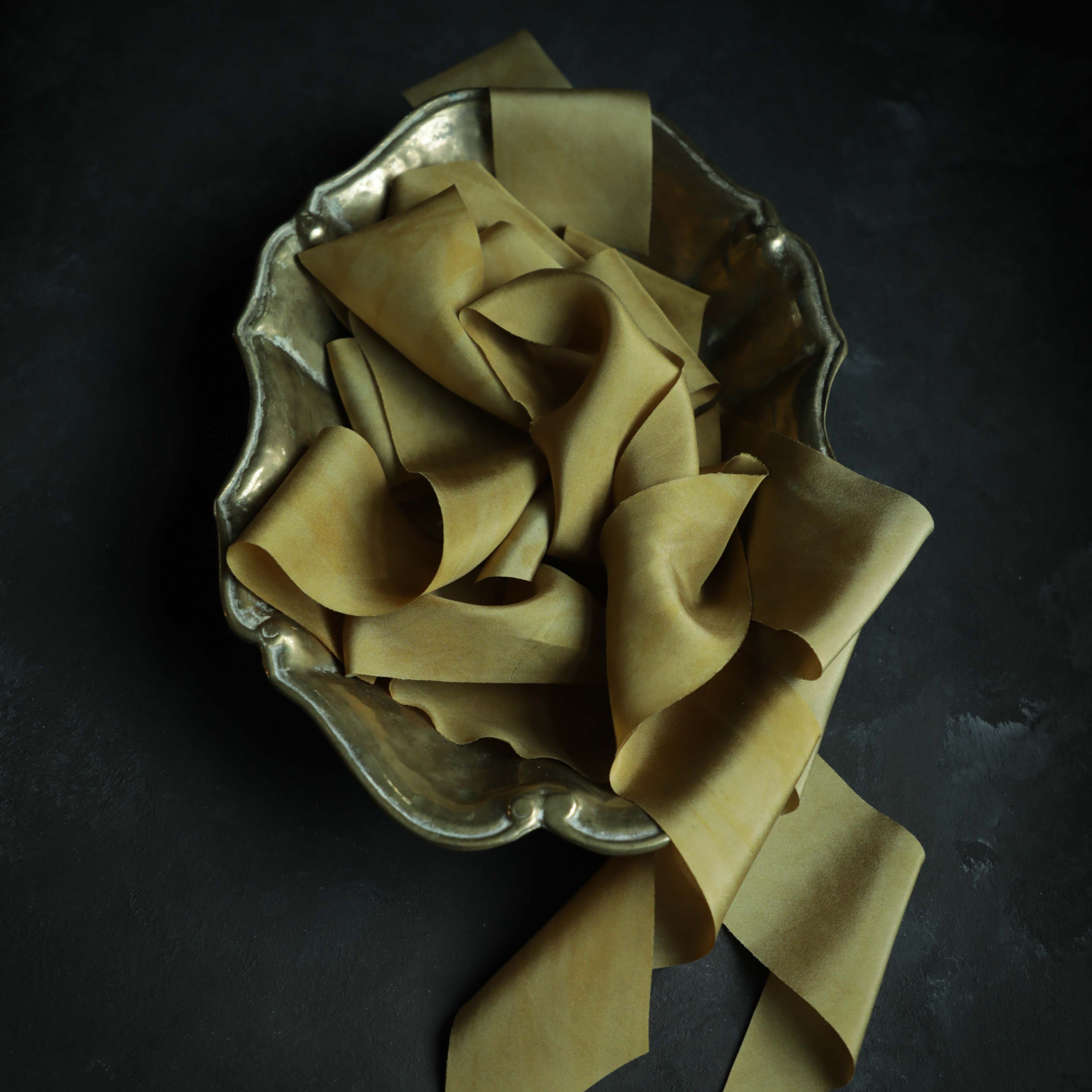 Plant-dyed silk ribbon displayed elegantly in a brass gold bowl, showcasing its luxurious sheen and soft hues, ideal for wrapping bridal bouquets. Perfect for brides-to-be, engaged couples, and florists seeking the world's finest ribbon for wedding flowers.