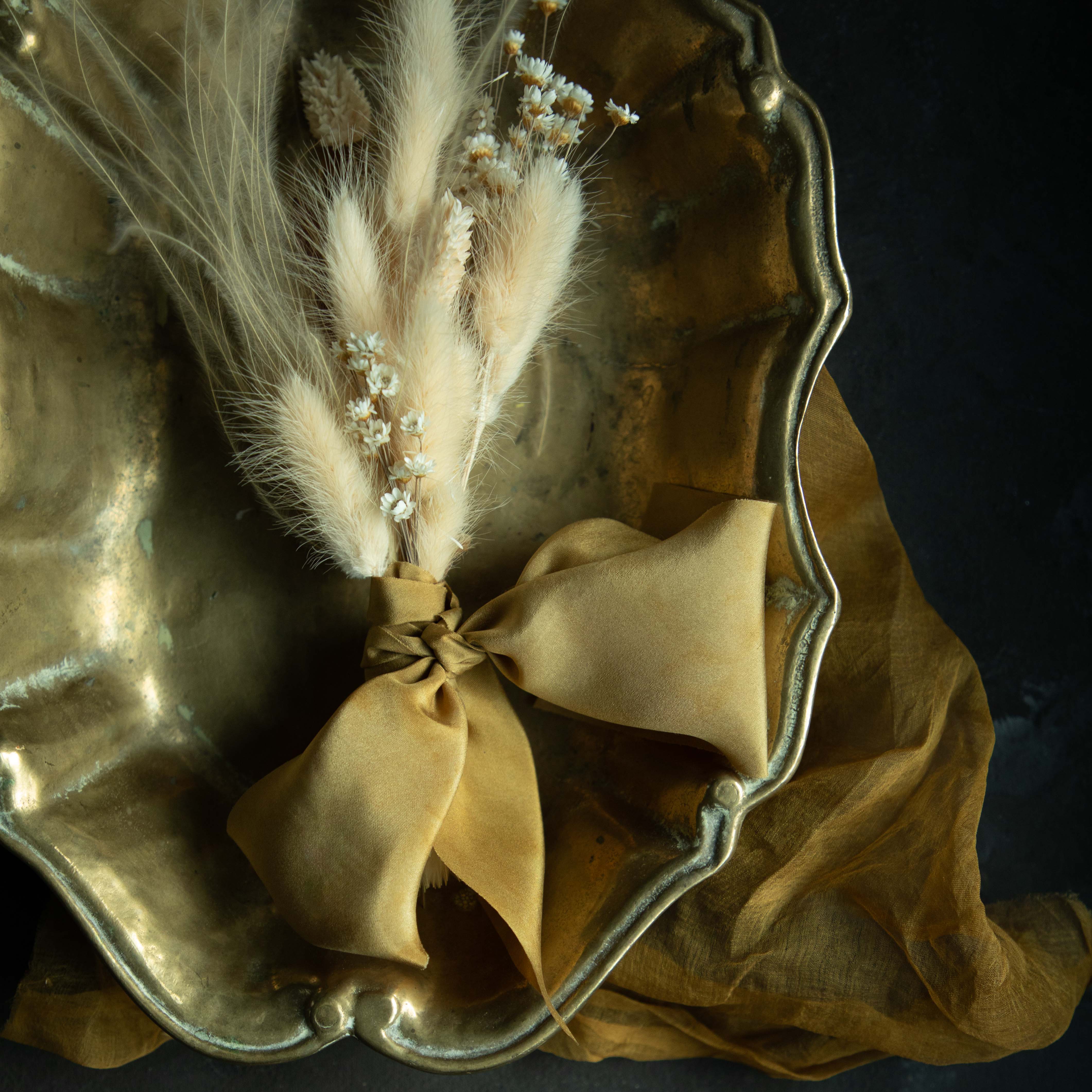 Plant-dyed silk ribbon displayed elegantly in a brass dish, showcasing its luxurious sheen and soft hues, ideal for wrapping bridal bouquets. Perfect for brides-to-be, engaged couples, and florists seeking the world's finest ribbon for wedding flowers.