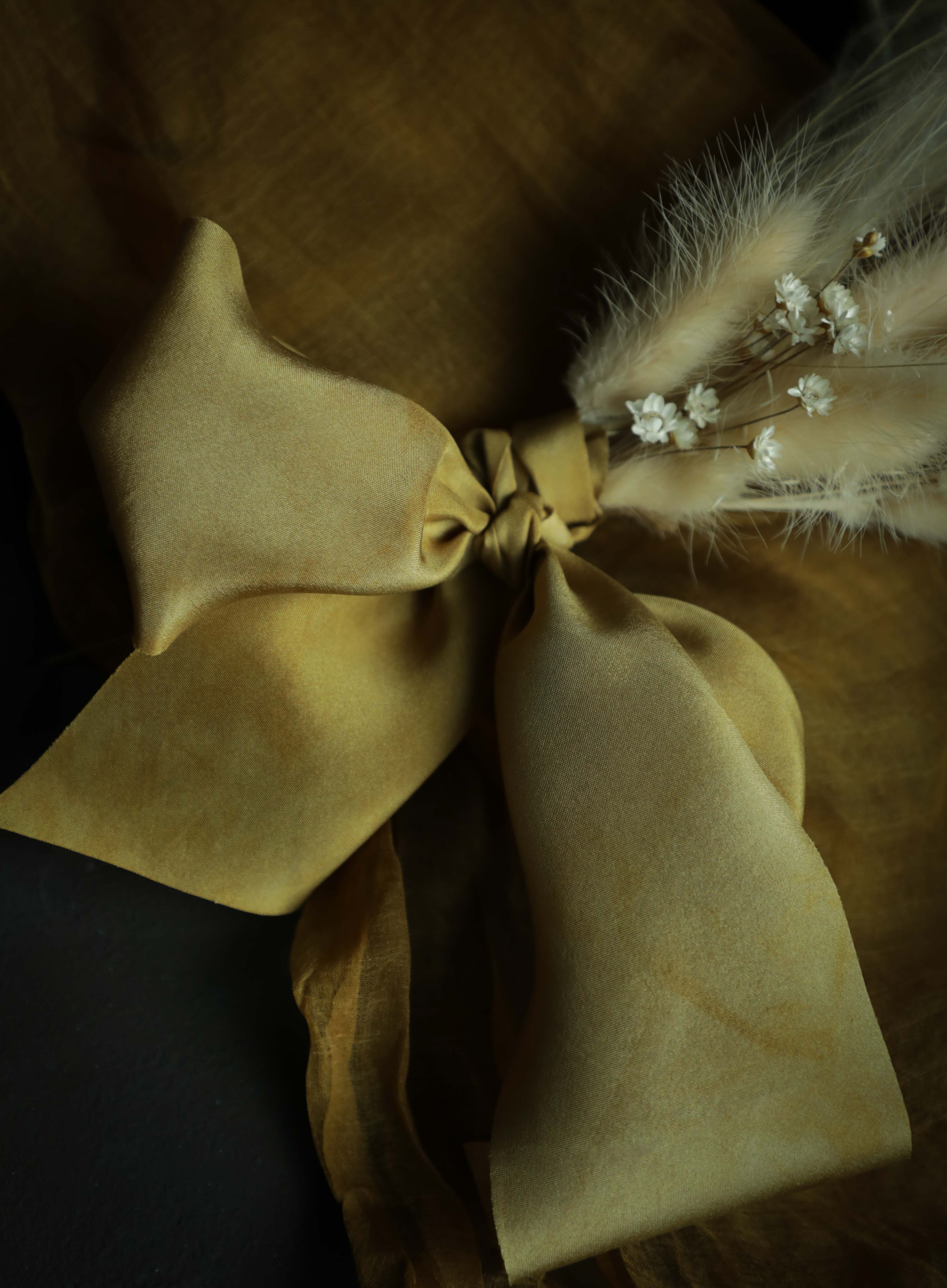 Gold plant-dyed silk ribbon displayed elegantly against a textured background, showcasing its luxurious sheen and soft hues, ideal for wrapping bridal bouquets. Perfect for brides-to-be, engaged couples, and florists seeking the world's finest ribbon for wedding flowers.