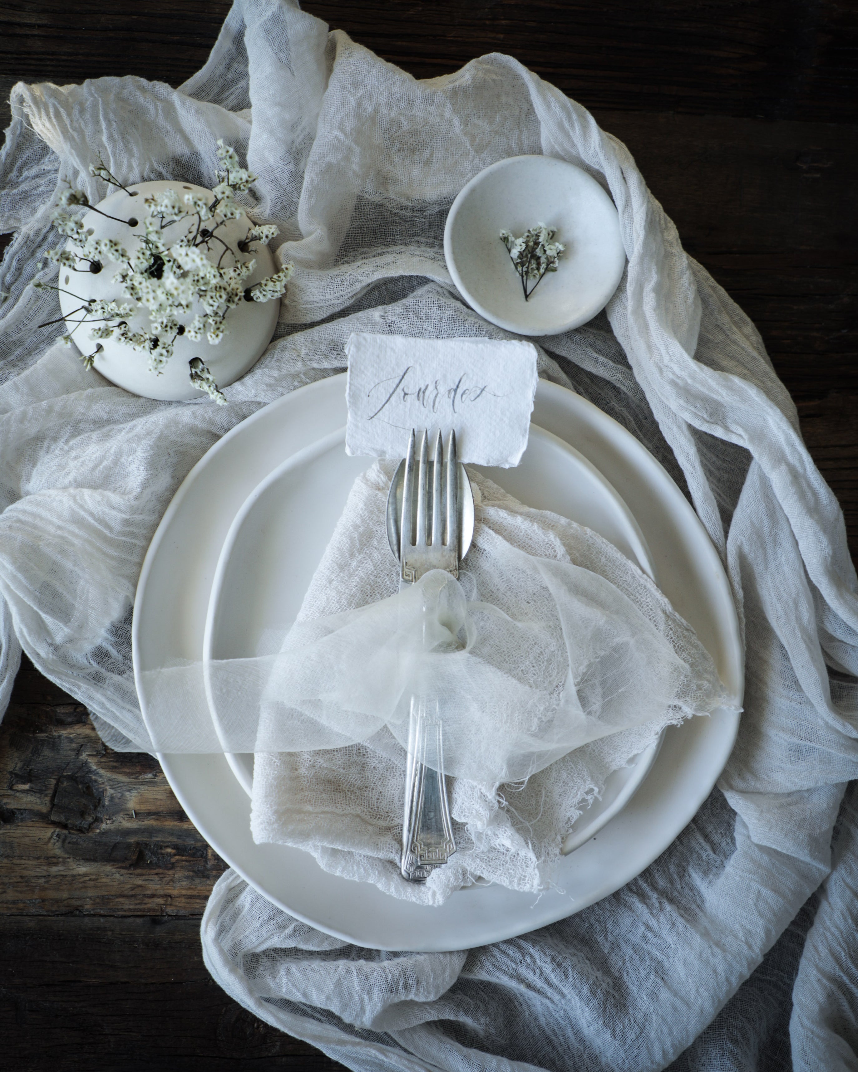 White theme tablescape with white napkins, white table runner, and white dried flower