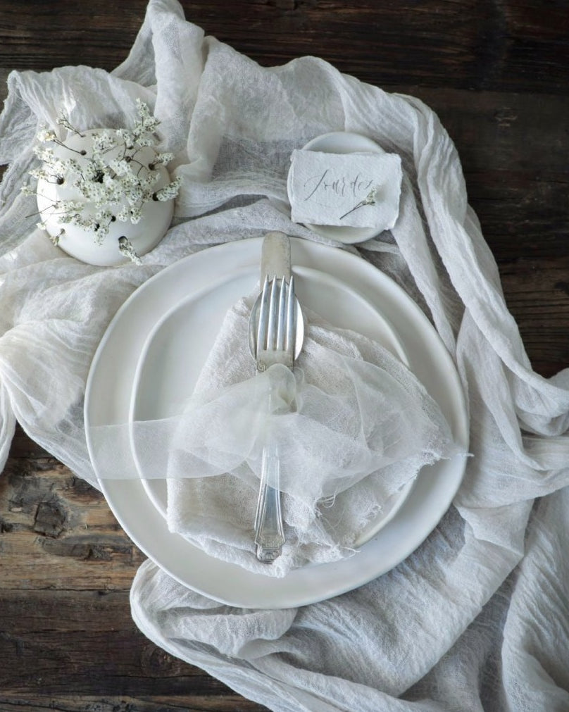 white theme table setting with white napkins, white table runner, and white silk ribbon tied on the flatware