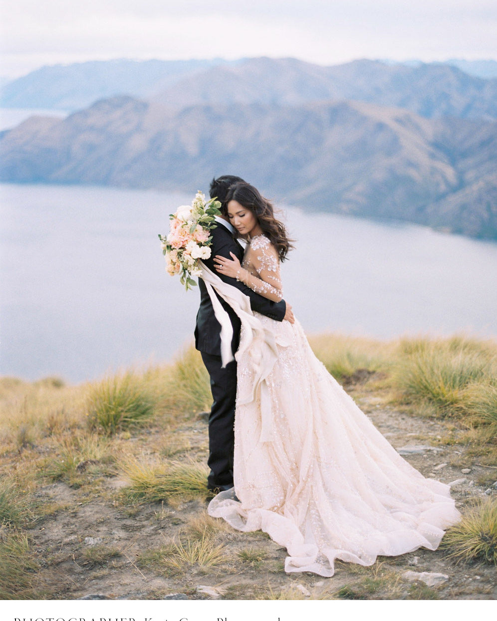 bride and groom hugging on New Zealand ridge with bridal bouquet and flowing silk and willow ribbon