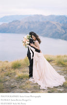 bride and groom hugging on New Zealand ridge with bridal bouquet and flowing silk and willow ribbon