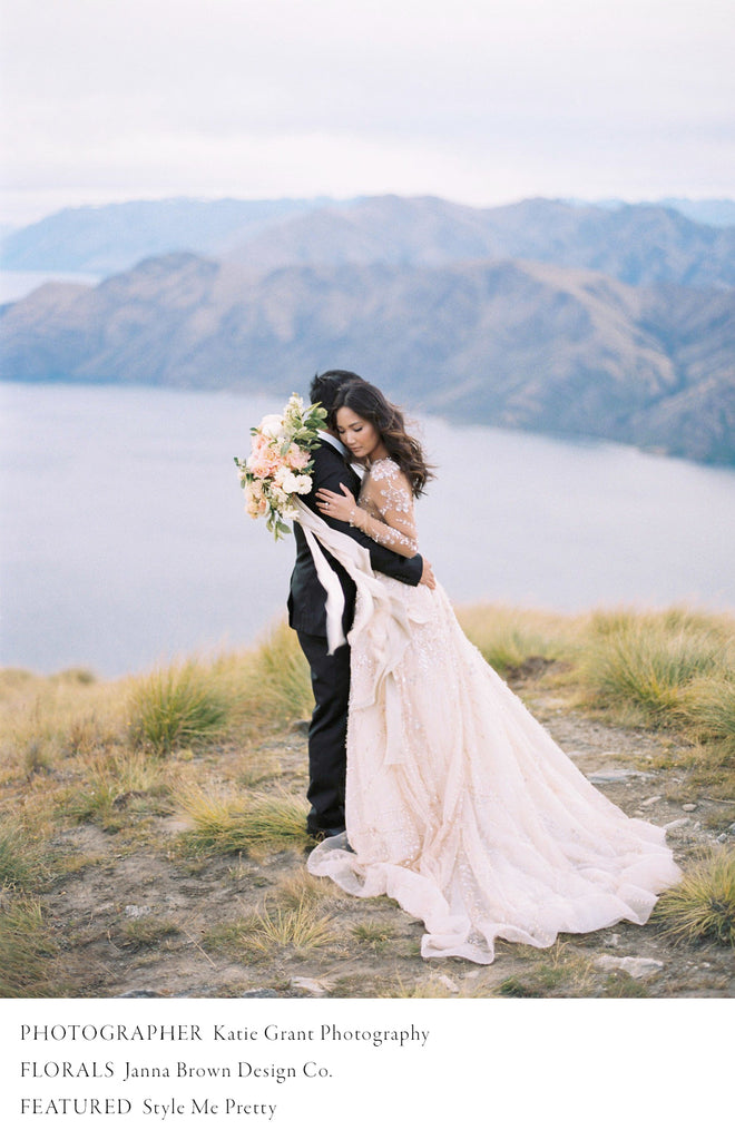 bride and groom hugging on New Zealand ridge with bridal bouquet and flowing silk and willow ribbon