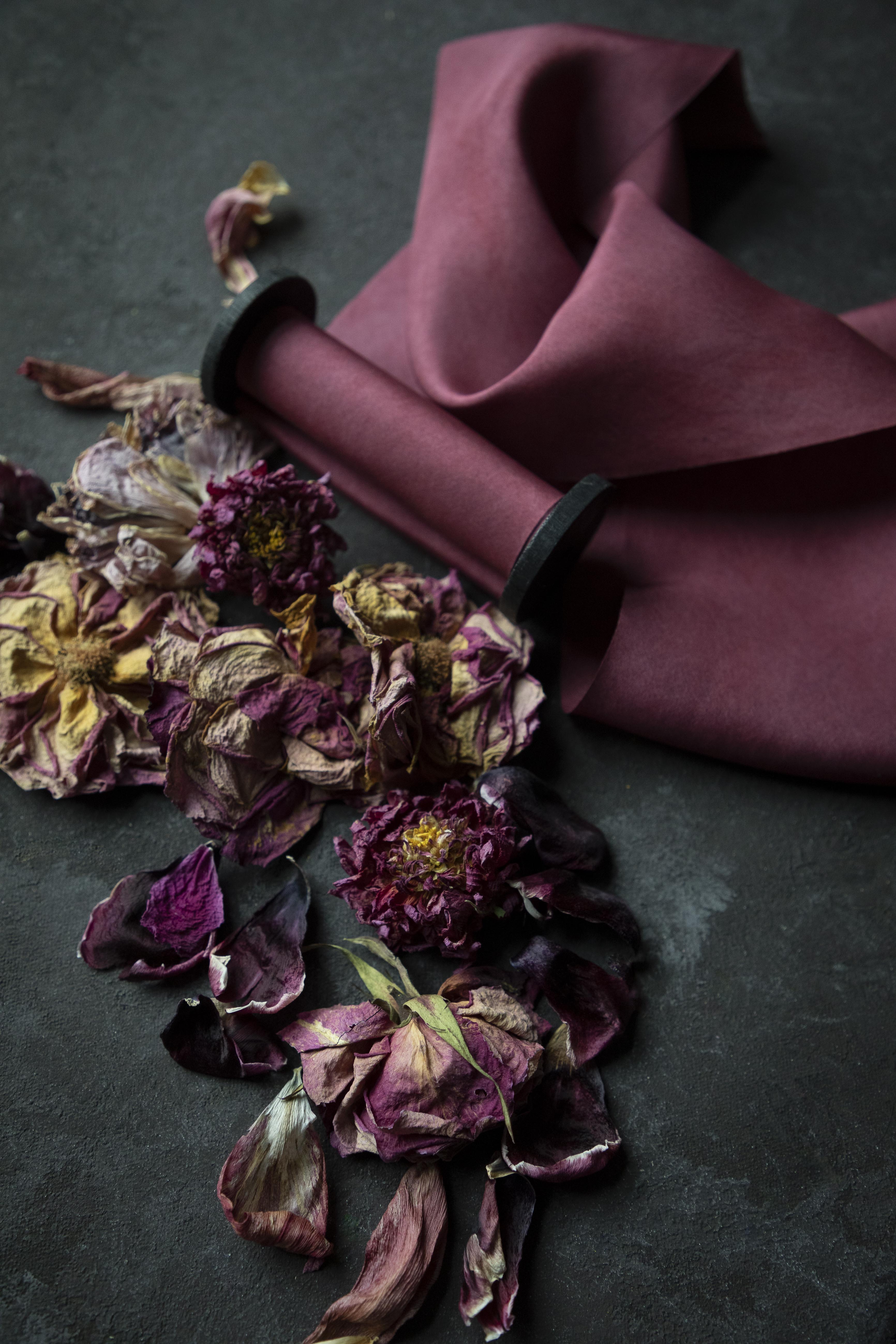 red silk ribbon on black textured surface next to dried rose petals